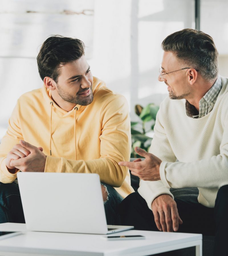 son and mature father sitting neat table with laptop and talking at home